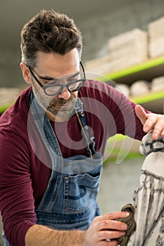 Portrait of Ceramist Dressed in an Apron Working on Clay Sculpture in Bright Ceramic Workshop. photo