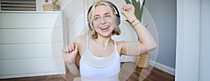 Portrait of charismatic, beautiful young woman dancing and listening to music in wireless headphones, singing along