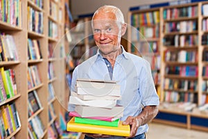 Portrait of charismatic older man in library with pile of books in hands