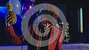 Portrait of a charismatic young man at birthday party take a pineapple and funny playing with a fructe