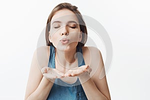 Portrait of charming beautiful young european woman with dark long hair and closed eyes, sending air kiss in camera with