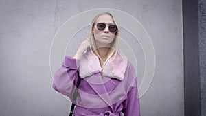 Portrait of a charming blonde girl in a purple coat and sunglasses, cold fall weather.