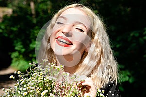portrait of a charming blonde teenage girl wearing teeth braces with bouquet of white wildflowers. female with braces in