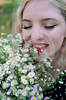 portrait of a charming blonde teenage girl wearing teeth braces with bouquet of white wildflowers. female with braces in