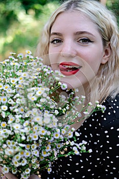 portrait of a charming blonde teenage girl wearing teeth braces with bouquet of white wildflowers. female with braces in