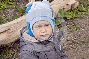 Portrait of a charming boy of two years with a serious facial expression in a hat and jacket on a background of nature.