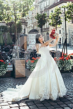 Portrait of the charming brunette with lovely smile raising up the wedding bouquet of red and pink flowers in the sunny