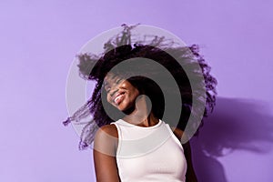 Portrait of charming cheerful dark skin girl closed eyes beaming smile flying hair isolated on purple color background