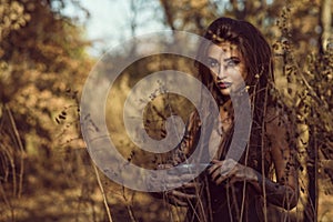 Portrait of charming dangerous young witch holding a pot with magic potion in the woods and looking straight with penetrating gaze photo