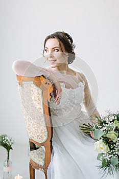 Portrait of a charming dark-haired bride sitting on the chair and holding bouquet of flowers, Studio, close-up. Wedding