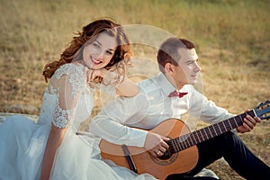 Portrait of the charming ginger hair bride with pretty smile enjoying the guitar play of her elegant groom while sitting