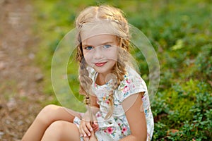 Portrait of charming girl with blonde pigtails, on the grass in