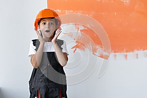 Portrait of a charming girl in an orange hard hat on her head. raised her hands to her face with an emotion of surprise.