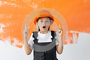 Portrait of a charming girl in an orange hard hat on her head. raised index fingers upward emotion of surprise.