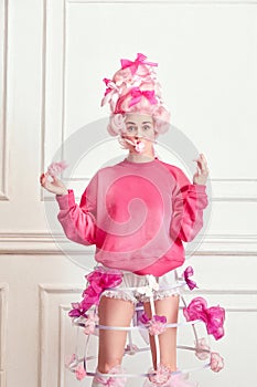 Portrait of charming girl, princess wearing pink wig and eating sweet cotton over luxury interior background. Sugar diet