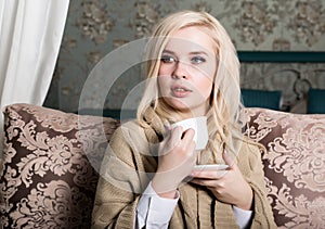 Portrait of charming girl in sweater sitting on a sofa and drinking tea or coffe