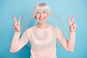 Portrait of charming grandparent with toothy smiling making v-sign wearing pastel jumper isolated over blue background