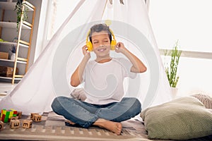 Portrait of charming happy small boy sitting floor listening music wear white shirt stylish child room interior