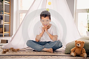 Portrait of charming happy small boy sitting floor playing smiling wear white shirt stylish child room interior