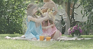 Portrait of charming happy twin sisters playing with soft toys on backyard. Caucasian brunette girls resting on sunny