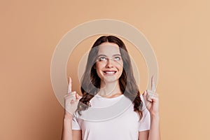 Portrait of charming interested girl indicate fingers up look empty space isolated on beige background