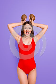 Portrait of charming lady in red swimsuit with coconut in hands above the head isolated on bright yellow background