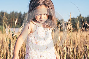 Portrait of charming little girl in light sundress made of natural fabric on summer day in field.