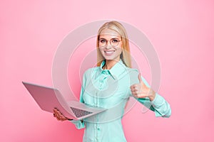 Portrait of charming manager holding gadget showing thumb up wearing teal shirt eyewear eyeglasses isolated over pink