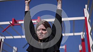 Portrait of charming motivated sportswoman doing pullups in slow motion looking away and smiling. Happy inspired