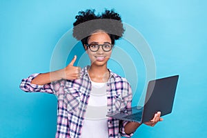 Portrait of charming positive teenager with afro hairstyle wear plaid shirt hold laptop showing thumb up isolated on