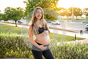 Portrait of charming pregnant woman touching her belly outdoors. Pregnancy, expecting baby, healthy lifestyle concept.