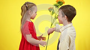 Portrait of charming pretty girl receiving bouquet of flowers from smiling loving boy. Surprised excited Caucasian child