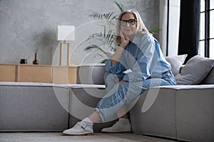 Portrait of charming senior woman with grey hair, smiling mature female sits on the couch and looks at the camera