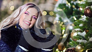 Portrait of charming smiling woman wearing amazing evening makeup posing near Christmas tree