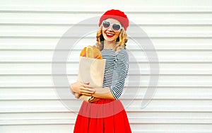 Portrait charming smiling woman wearing french red beret holding paper bag with long white bread baguette on white