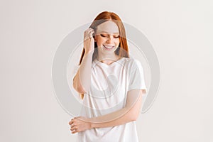 Portrait of charming smiling young woman touching playfully red hair looking down, on white isolated background in