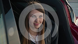 Portrait charming woman sitting inside charging electric car. young modern girl looks from the phone to the camera and