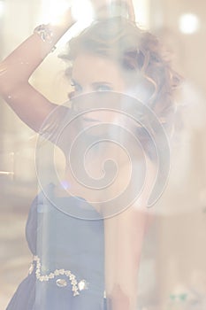 Portrait of a charming woman with stylish curly hairstyle wearing a blue dress posing next to a mirror. Beauty, vogue