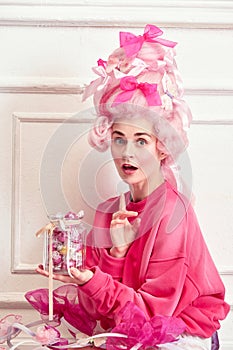 Portrait of charming young girl, princess wearing pink wig and eating candies, sweets over luxury interior background