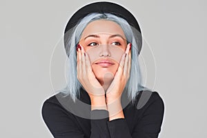 Portrait of charming young teenager woman with blue hair wearing black apparel and hat, smiling, looking up. Cute positive female