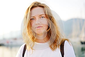 Portrait of charming young tourist woman on the Mediterranean coast. Attractive red-haired girl hiking by the sea shore