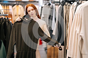 Portrait of charming young woman choosing clothes and looking to mirror in clothing store.