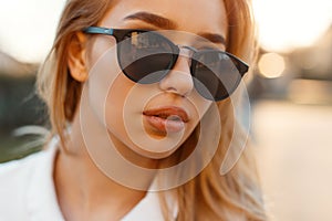 Portrait of a charming young woman with lips in black stylish sunglasses on sunset background. Attractive girl. Close-up.