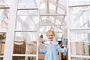 Portrait of cheerful 3-year-old toddler girl in beautiful dress standing posing in summer gazebo on sunny day smiling