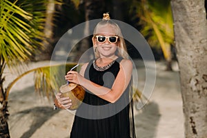 Portrait of a cheerful 9-year-old girl with a coconut cocktail on the background of palm trees on an exotic beach.little