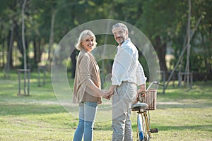 Portrait of cheerful active senior couple with bicycle walking through park together. Perfect activities for elderly people in