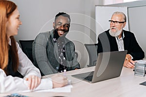 Portrait of cheerful African-American businessman sitting at table, sharing project ideas with mixed race investors at