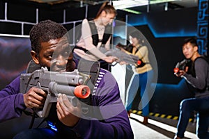 Portrait of cheerful African-American with laser gun having fun on dark laser tag arena