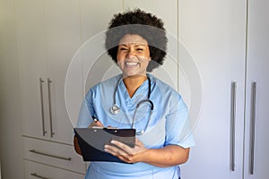 Portrait of cheerful african american mid adult female nurse with stethoscope writing on clipboard