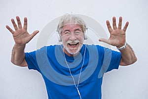Portrait of a cheerful and amused senior man wearing blue shirt while listening to music with headphones. Retired people on a